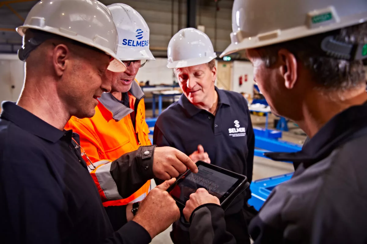 Team van engineers in een productieomgeving bekijkt samen operationele data op een tablet