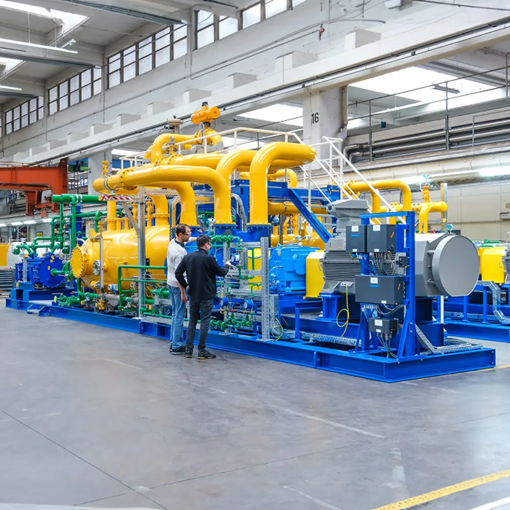 Twee technici controleren een geel-blauwe machine-installatie in een fabriekshal
